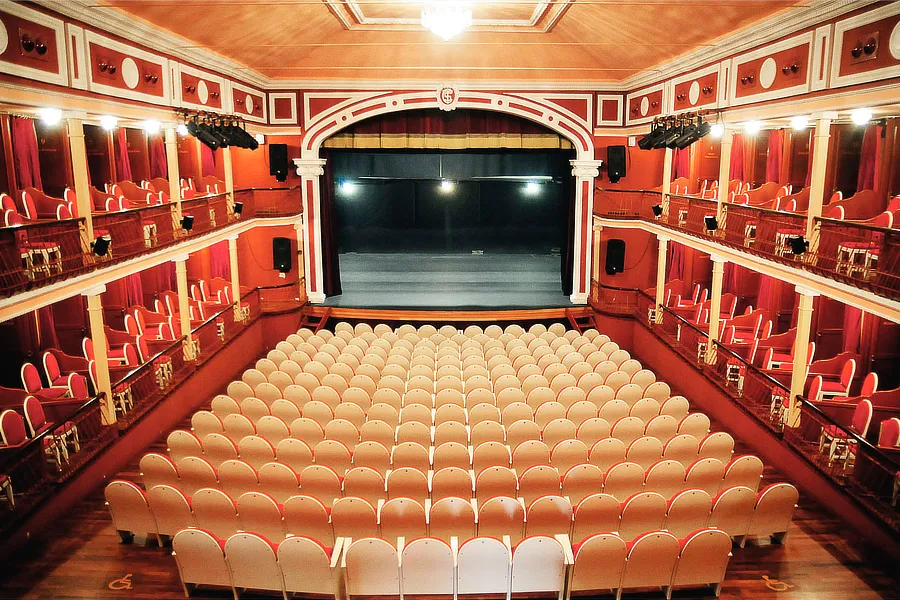 Vista interior del Teatro Salón Cervantes en Alcalá de Henares, con sus asientos vacíos y el escenario iluminado, preparado para una representación del Festival de Clásicos en Alcalá 2024