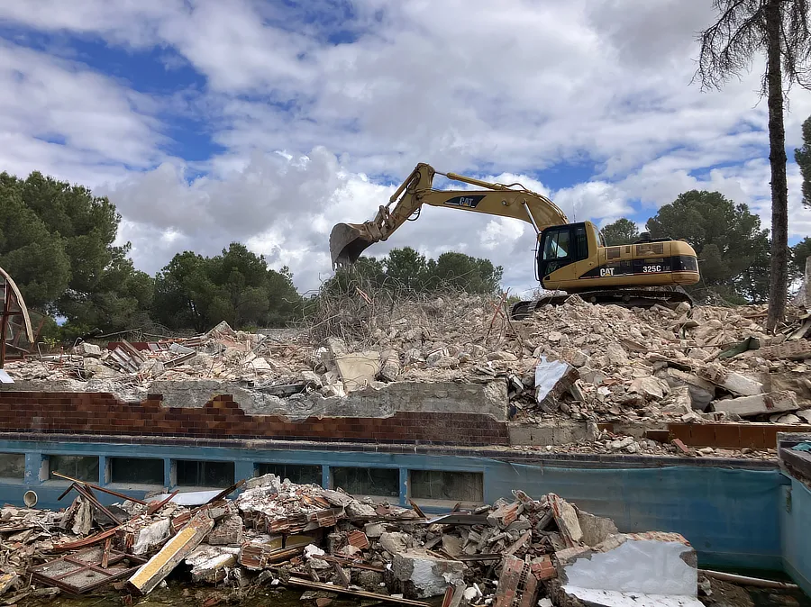 Vista de la excavadora demoliendo el chalet. junto a la piscina