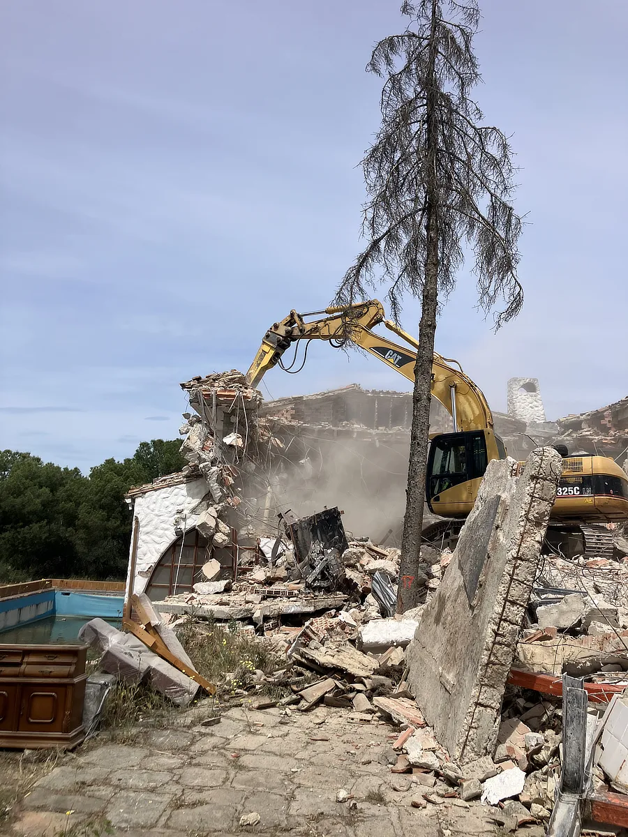 Vista de la excavadora demoliendo el chalet. Sobre algunos escombros.