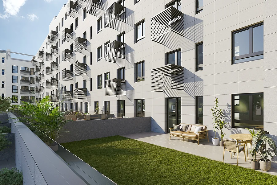 Un moderno edificio de pisos de varias plantas con una fachada blanca y balcones con diseños geométricos. La planta baja cuenta con un amplio jardín con césped bien cuidado y un patio con sofás y sillas. Las ventanas son grandes y permiten una abundante entrada de luz natural.