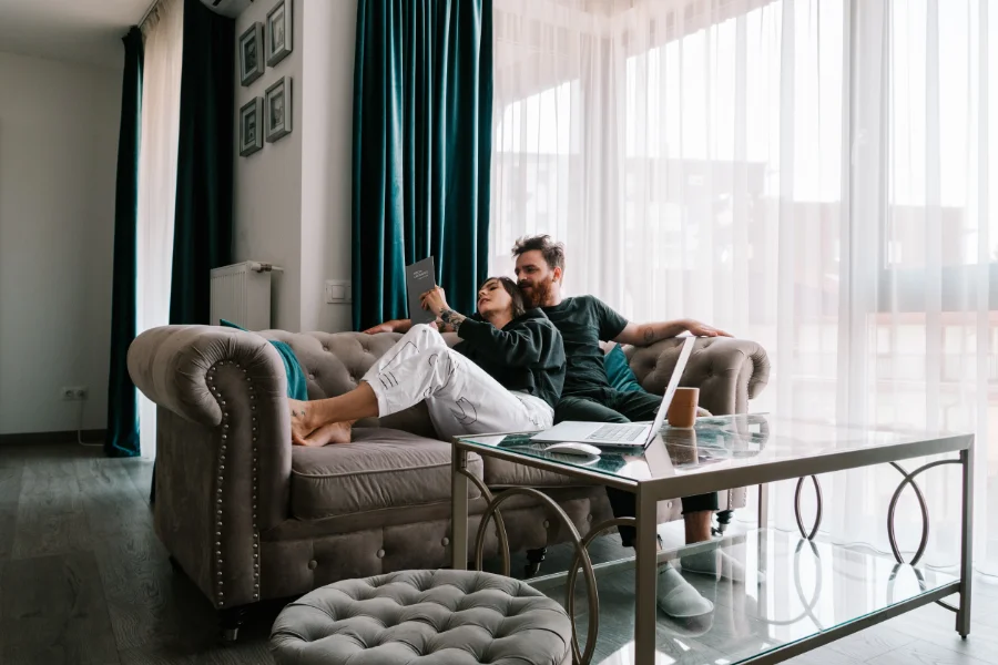 Una pareja compuesta por una mujer y un hombre están sentados en el salón de su nueva casa leyendo juntos lo que parece una escritura de compra de una vivienda