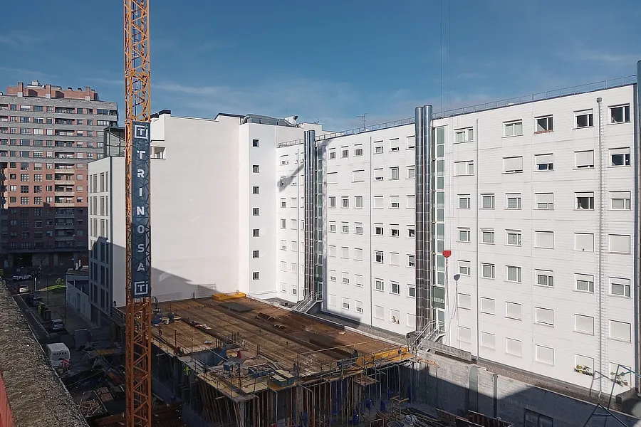 Vista de la base del edificio en construcción Tu Casa en Amézola. Promoción de obra nueva que está desarrollando Grupo Trinosa en Bilbao. Se puede ver la parte central de una grúa con una pancarta de Trinosa en el lado izquierdo de la foto y en el centro la base del edificio en construcción.