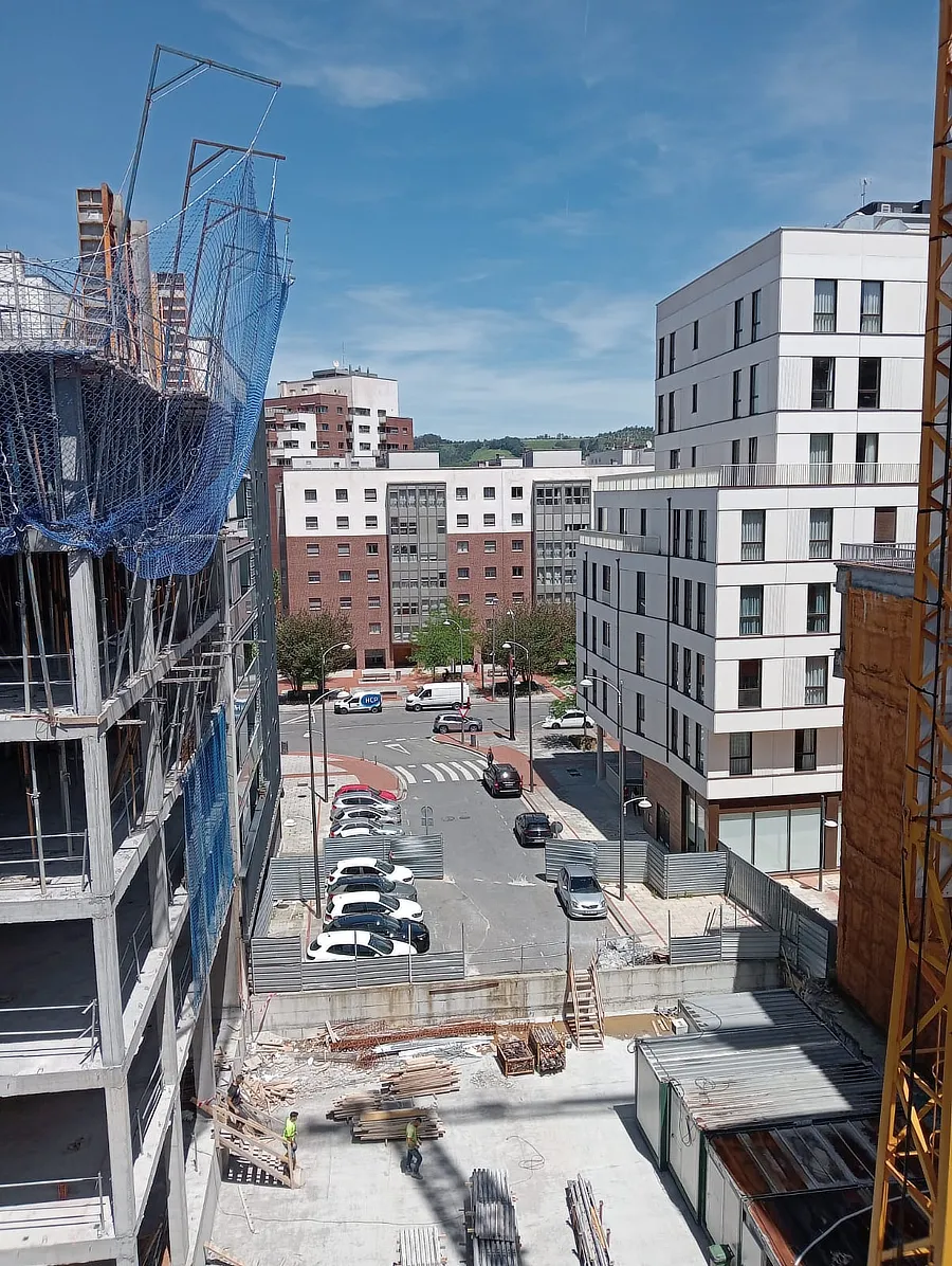 Vista de la otra parte de la fachada del edificio en construcción de Tu Casa en Amézola. Se observa la estructura de concreto y las redes de seguridad, con una grúa y un cielo despejado de fondo.