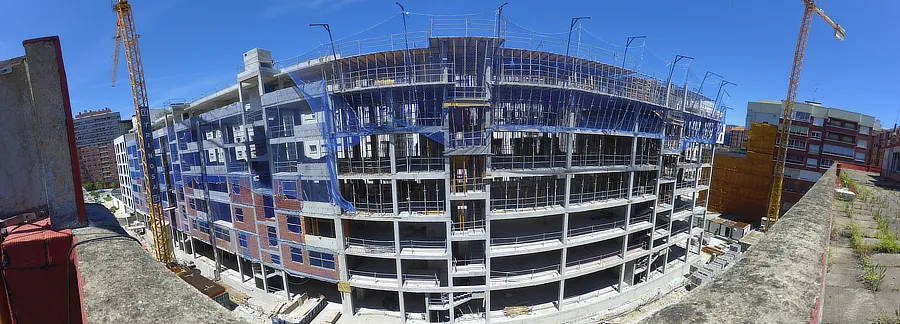 Imagen panorámica de la fachada larga del edificio en construcción de Tu Casa en Amézola. Se observa la estructura de concreto con redes de seguridad en los niveles superiores y varias grúas en funcionamiento.